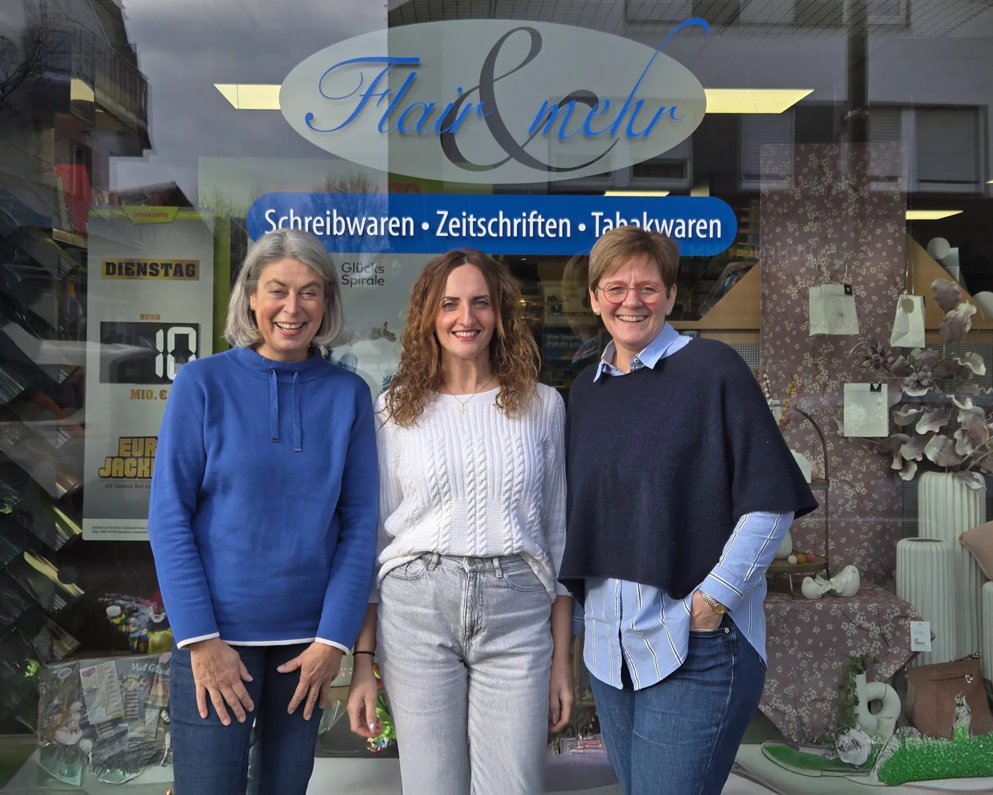 Drei Mitarbeiterinnen von Flair &amp; mehr vor dem Schaufenster des Ladens, daneben Plakate von WestLotto und ein Schild mit Schreibwaren, Zeitschriften und Tabakwaren
